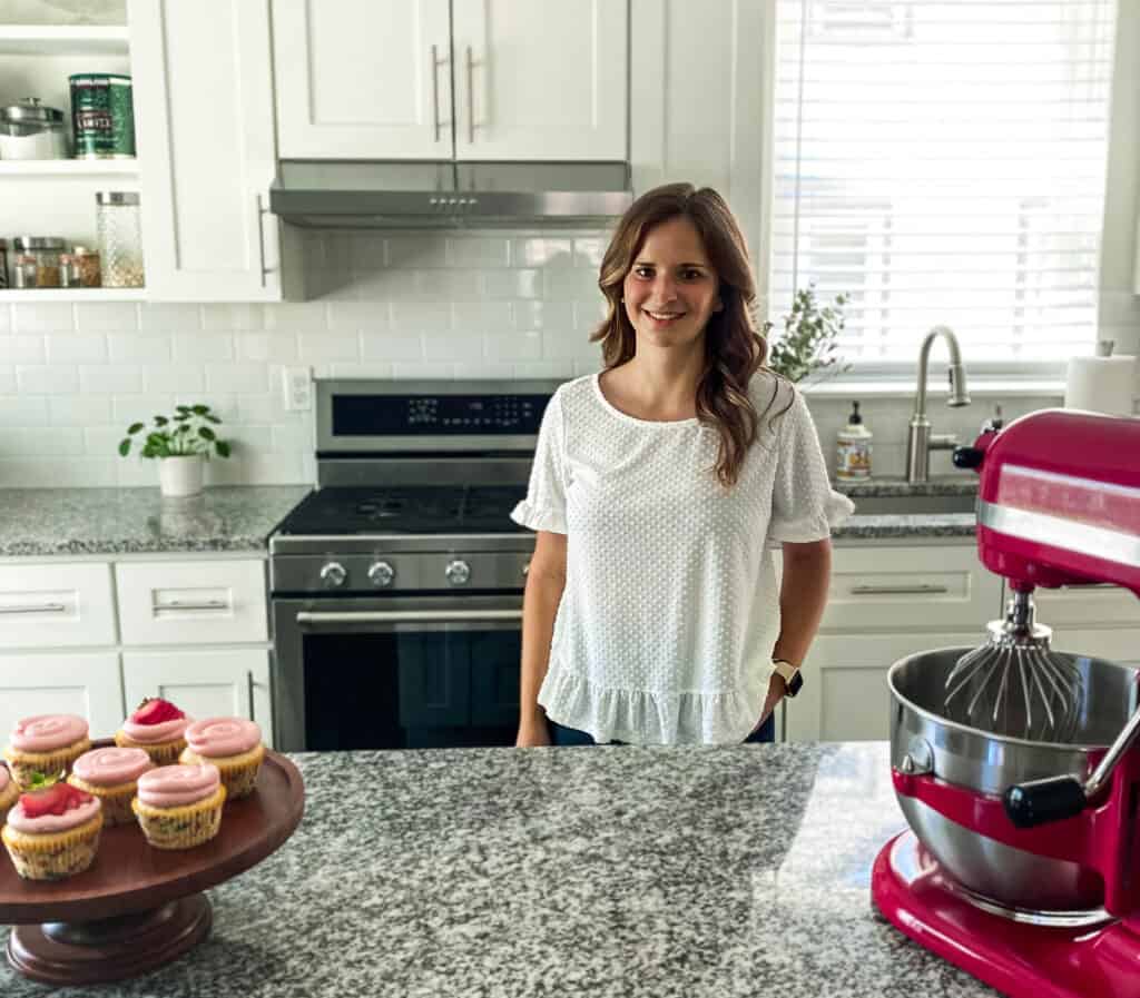 Alana in her kitchen with a mixer and almond cupcakes with strawberry frosting