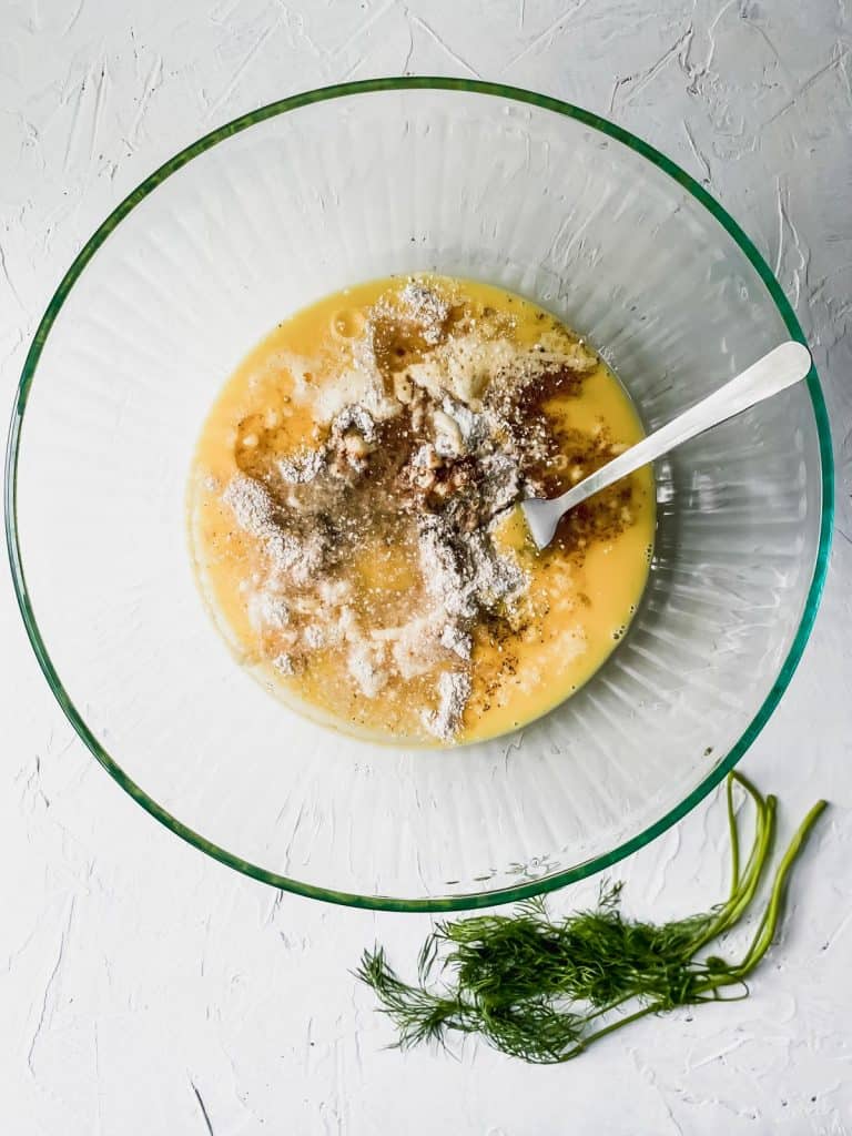 All matzo ball ingredients combined in a glass bowl with dill on the side