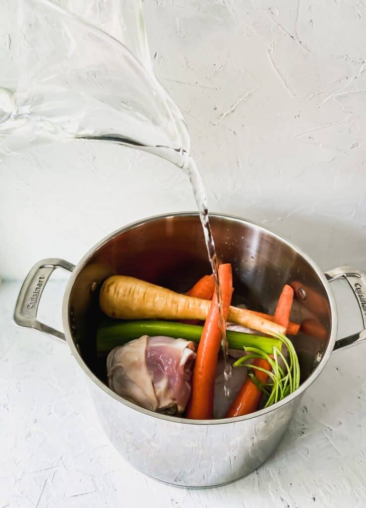 Pouring water into a metal pot full of soup ingredients