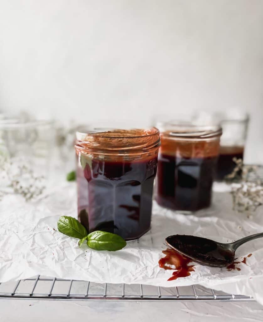 pomegranate bbq sauce in jars with a spoon covered in sauce