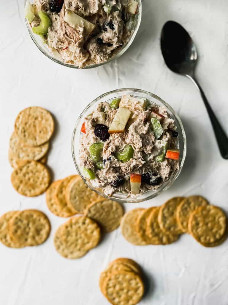 2 glass bowls of chicken salad with a spoon and crackers around them