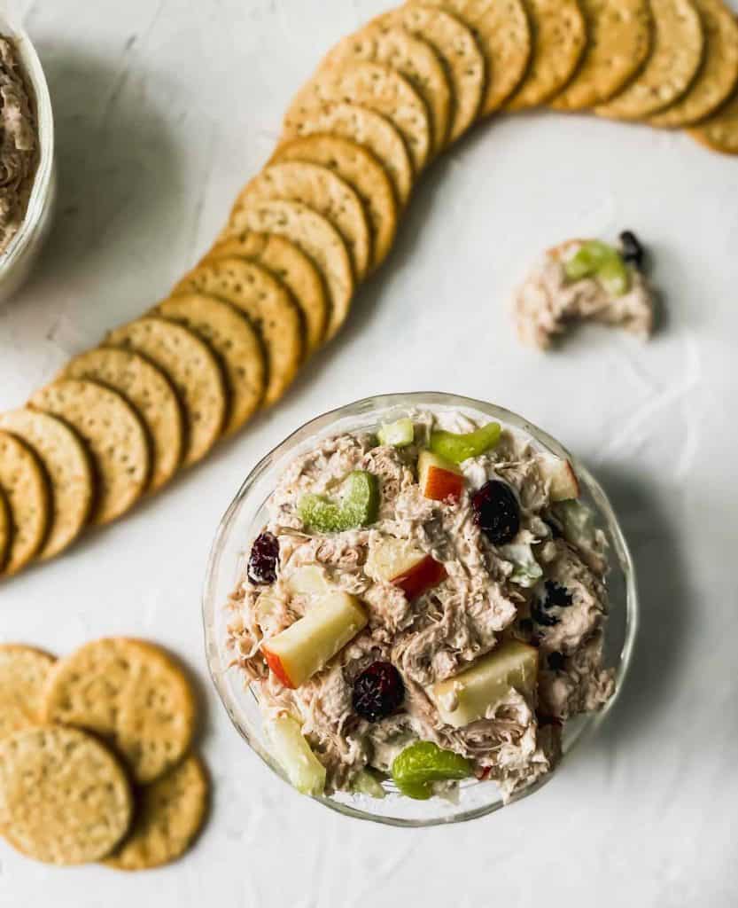 shredded chicken salad with cranberries and apples in a glass bowl with crackers around it