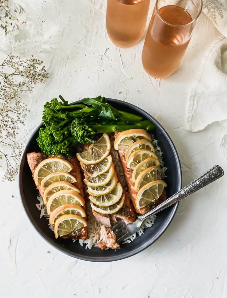 baked teriyaki salmon in a black bowl with 2 glasses of rosé wine next to it.