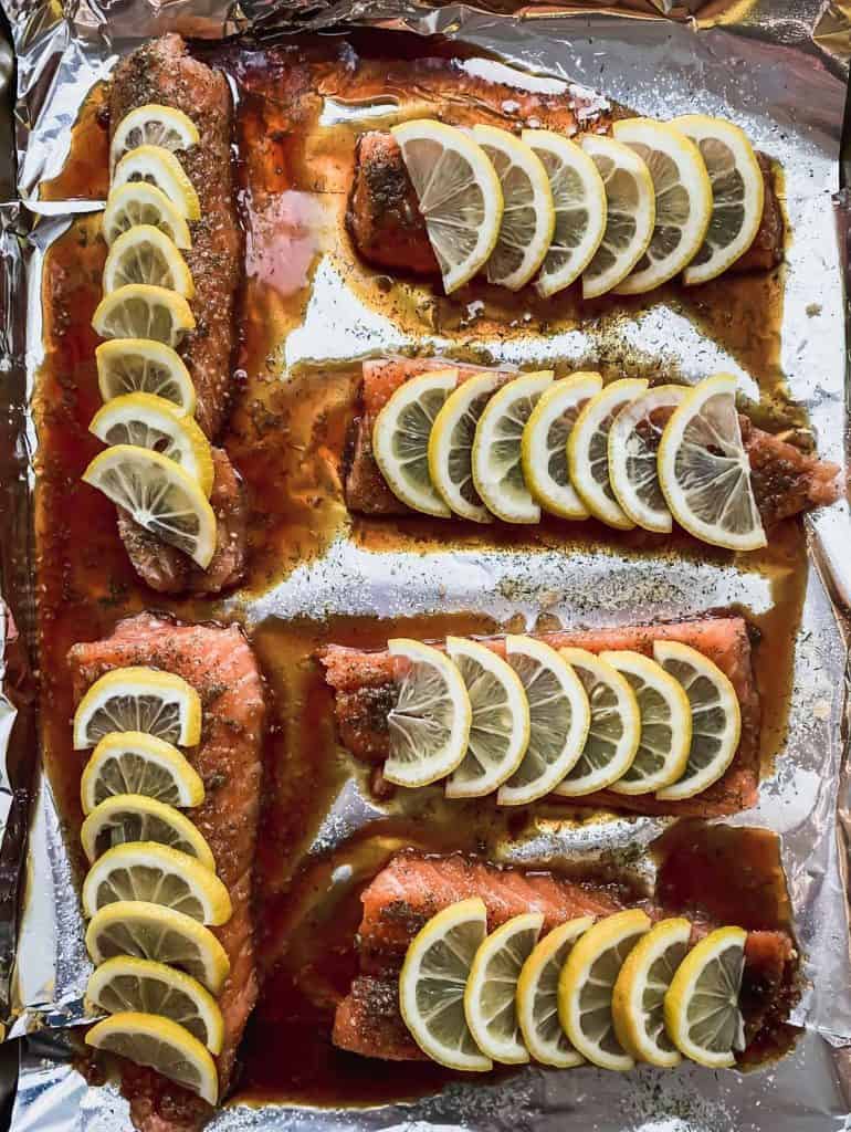 6 fillets with seasonings, sauce, and lemon slices on a foil lined sheet pan.