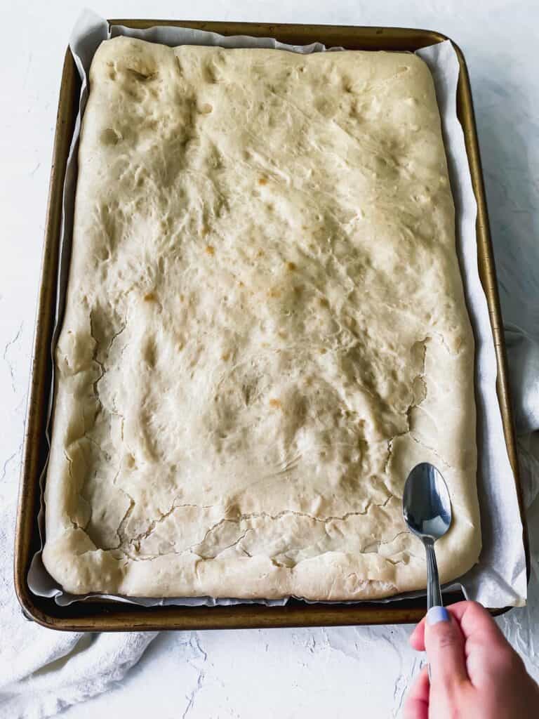 using a spoon to tamp down the middle of the baked pizza dough