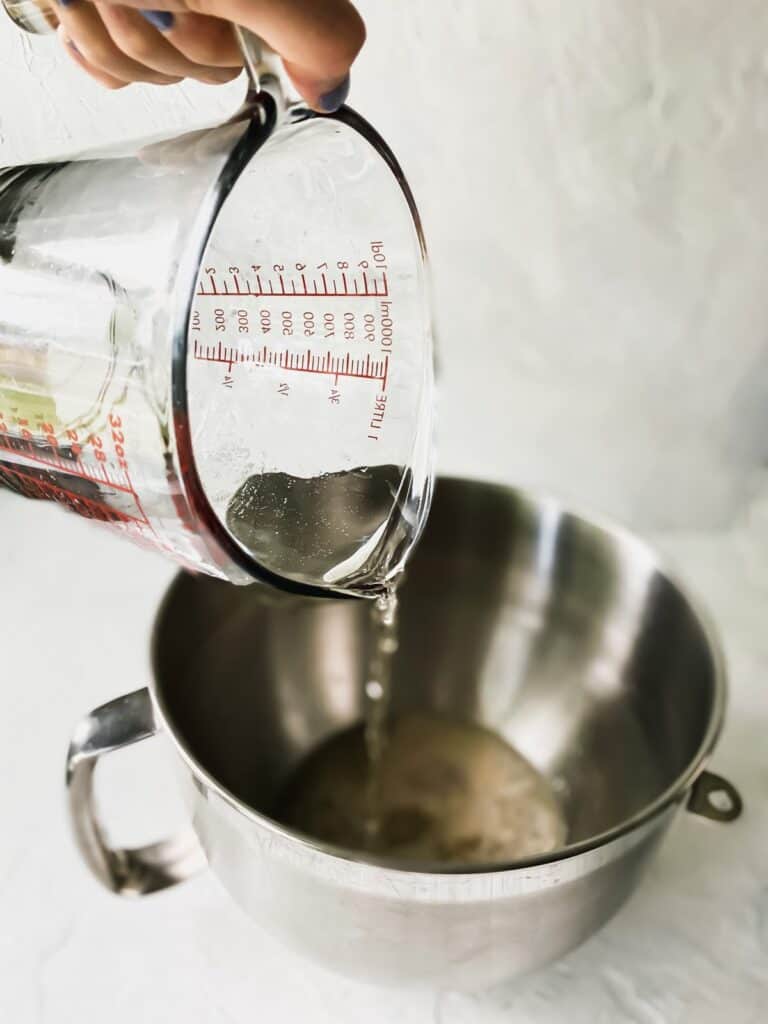 pouring warm water into a mixing bowl with yeast and beer